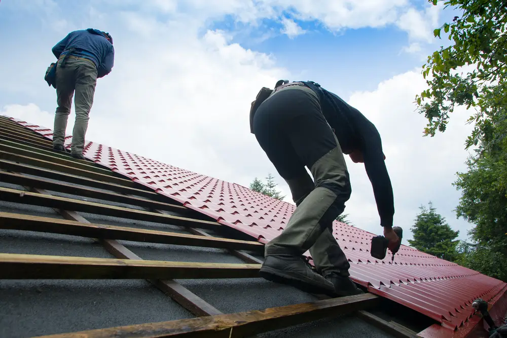 Roofer installing red metal roofing panels