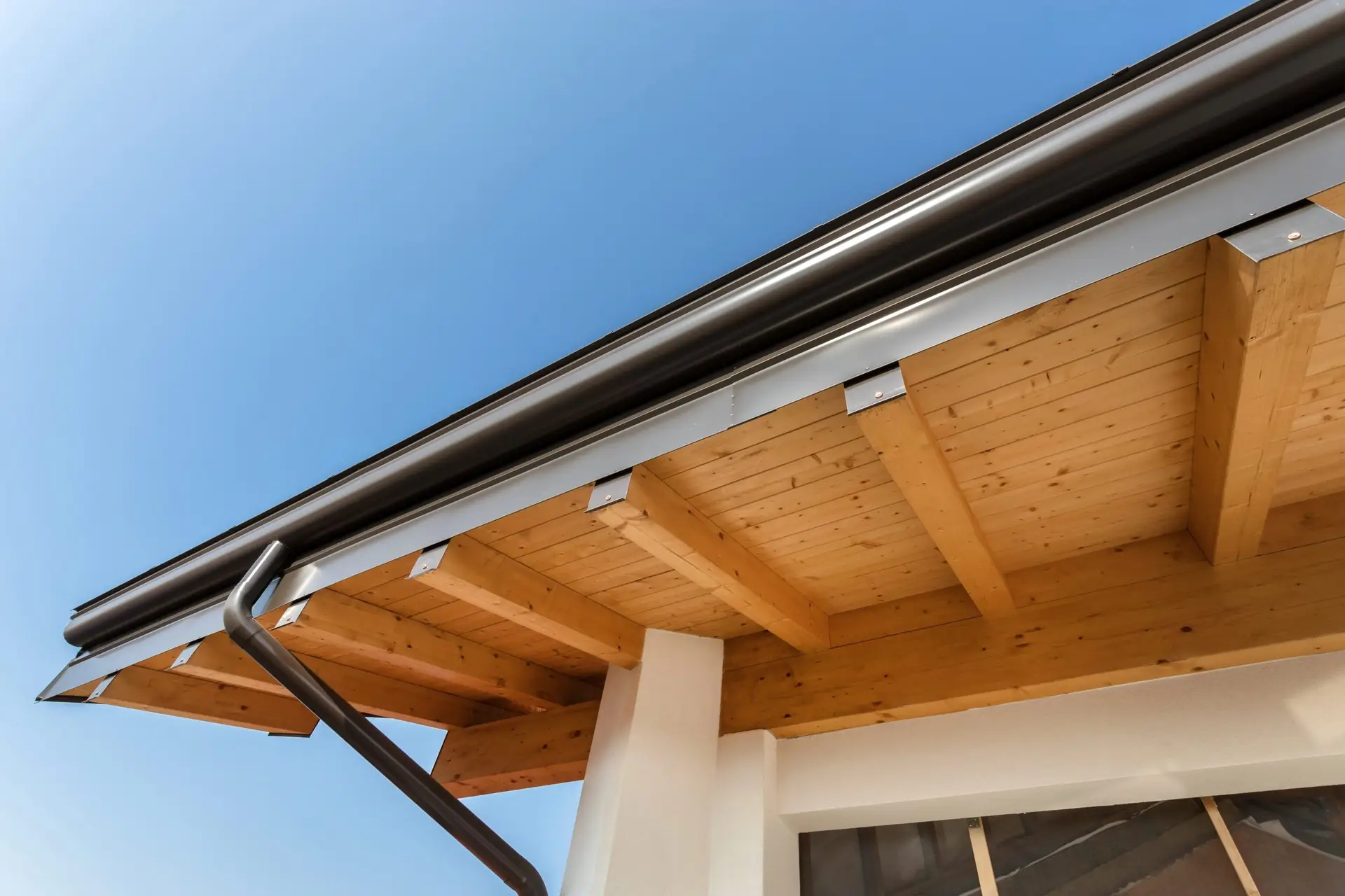 Roof eave with wood soffit and gutter against a blue sky